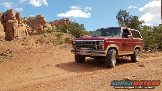 Red Ford Bronco parked on a dirt road with red rock formations in the background