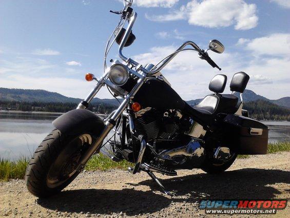 Black motorcycle with chrome handlebars and dual seats parked by a lake