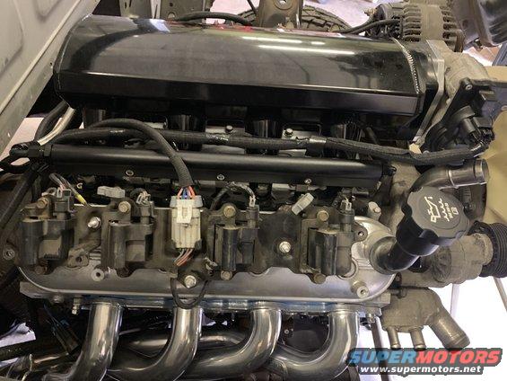 Close-up of an engine block with chrome headers, fuel injectors, and ignition coils. Oil cap visible