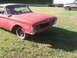 1960 Ford Starliner - This red 1960 Ford Starliner is missing its grille and shows signs of wear, parked in a grassy area with other vehicles visible.