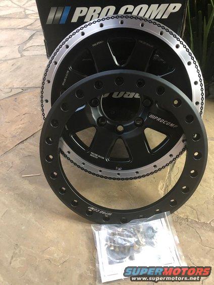 Two black Pro Comp wheels with silver beadlock rings and hardware on a stone surface