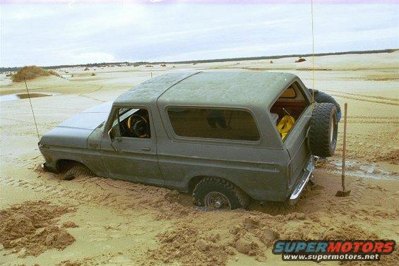 Gray 1978 Ford Bronco stuck in sand dunes, spare tire mounted on rear door