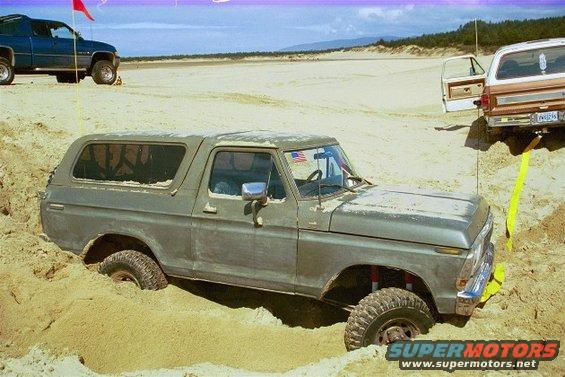 Gray Ford Bronco stuck in sand dune, another SUV and pickup truck visible in background