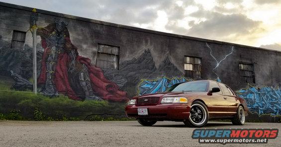 Maroon sedan with black rims parked in front of a graffiti mural on a brick wall