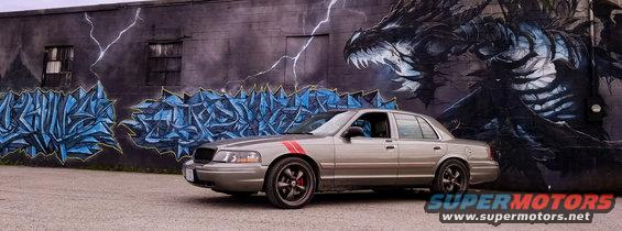 Tan 2004 Ford Crown Victoria with red racing stripes parked in front of a dragon mural