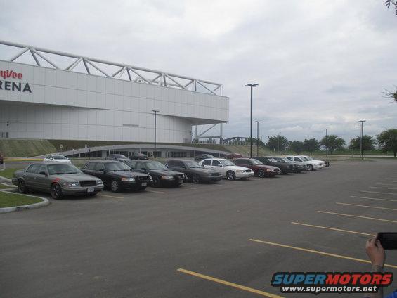 Several Ford Crown Victoria police cars parked in a lot in front of a large arena