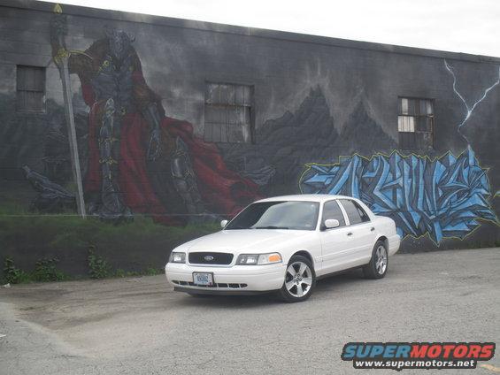 White 2004 Ford Crown Victoria parked in front of a mural of a knight and graffiti