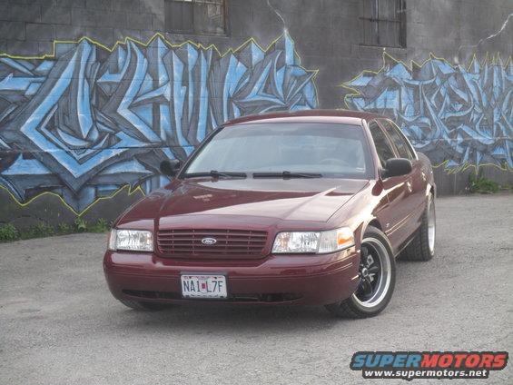 Maroon Ford Crown Victoria parked in front of graffiti wall. License plate NA1-L7F