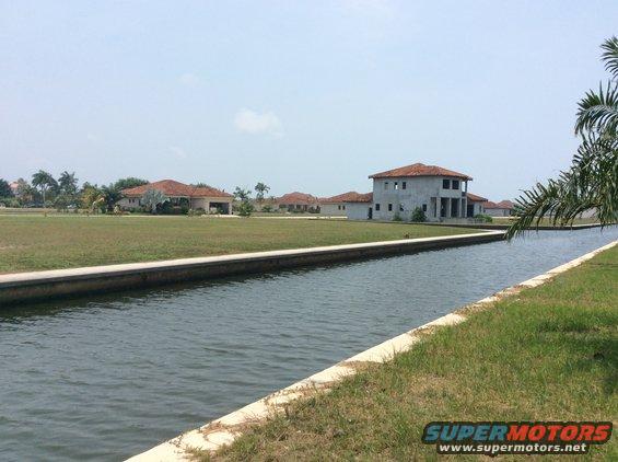 Water canal with grassy banks and houses under construction in the background