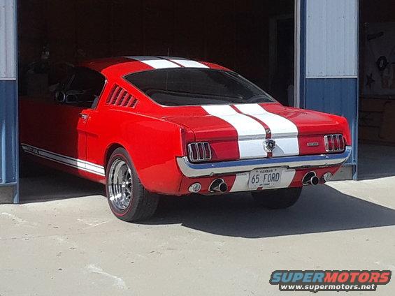Red 1965 Ford Mustang fastback with white stripes parked in a garage
