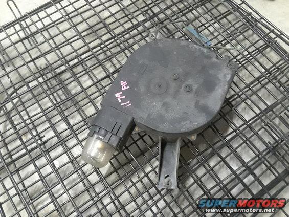 Black automotive part with a clear bulb, resting on a metal rack. Pink writing on the part reads '11 79 PP'