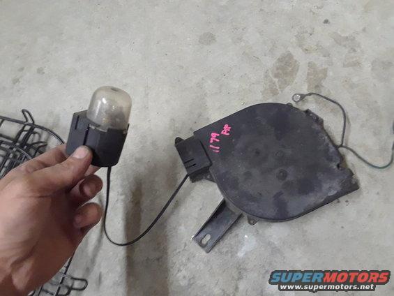 Black plastic automotive part with a clear dome and wiring, next to a larger black component with pink writing