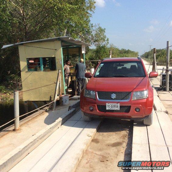 Red Suzuki Grand Vitara parked on a wooden bridge, with a small yellow booth to the left