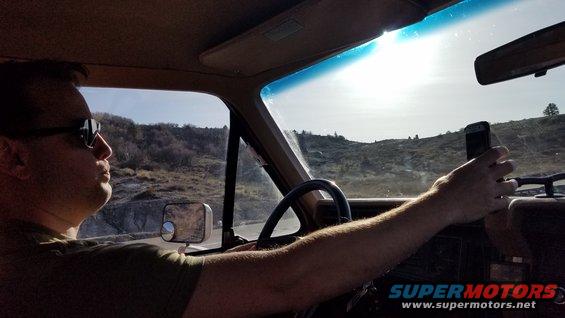 1985 Ford Bronco interior, driver holding phone, sunny day