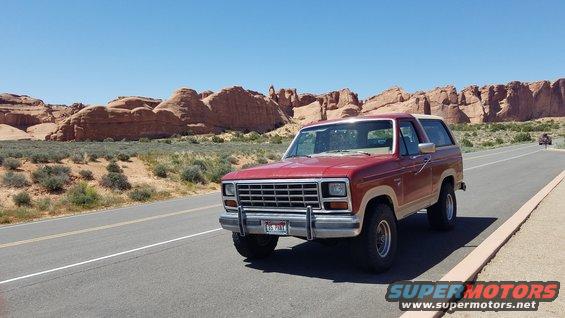 Red Ford Bronco parked on the side of a road with red rock formations in the background