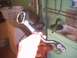 1991 Ford Crown Victoria - A chrome-plated metal part, possibly a linkage or lever, is held in a hand against a background of a laundry basket and plumbing.