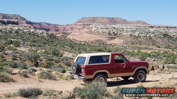 Red 1985 Ford Bronco parked on dirt road in desert with red rock formations in background