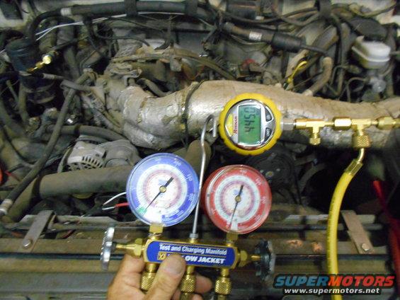 Engine bay with AC manifold gauges attached to hoses. Digital gauge reads 445.0