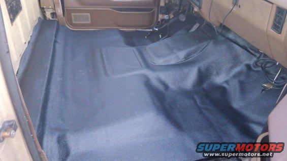 Dark vinyl flooring covers the interior floor of a vehicle, with visible door panel and dashboard elements