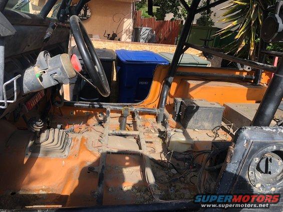 Interior of an off-road vehicle with orange floor, roll cage, and steering wheel. Trash cans visible outside