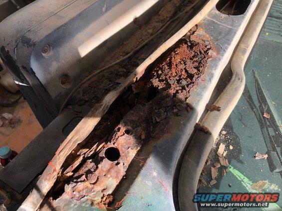 Close-up of severely rusted metal frame on a vehicle, showing extensive corrosion and flaking