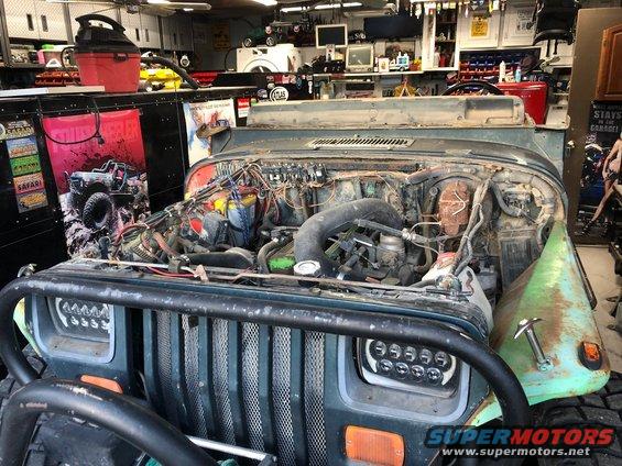 Green 1992 Jeep Wrangler with engine exposed, aftermarket headlights, and a rusty fender