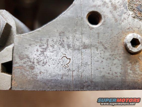 Metal part with a stamped clover-like symbol and vertical lines