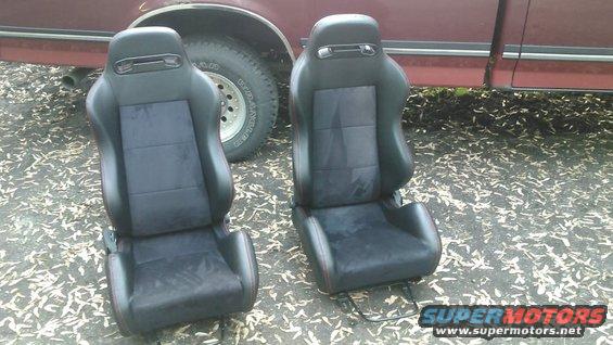 Two black racing seats with red stitching, parked next to a red vehicle