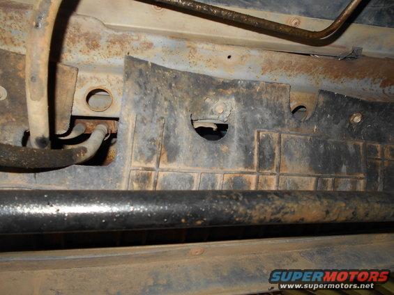 Underside of vehicle showing rusty frame, fuel lines, and a black plastic shield