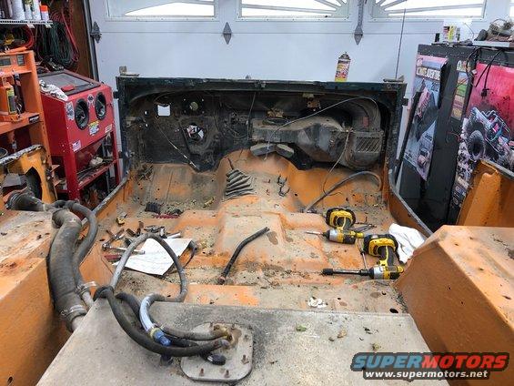 Interior of a stripped Jeep showing the floor pan, dashboard, and center console area with tools
