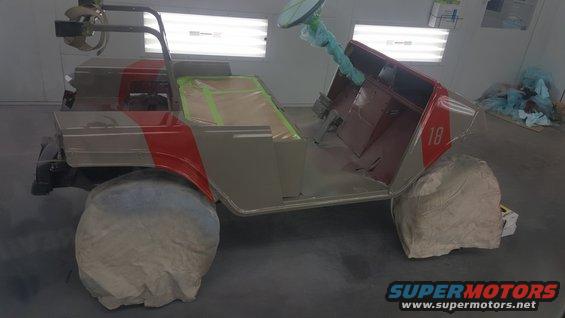 Golf cart with red and silver paint scheme, covered wheels, in a paint booth