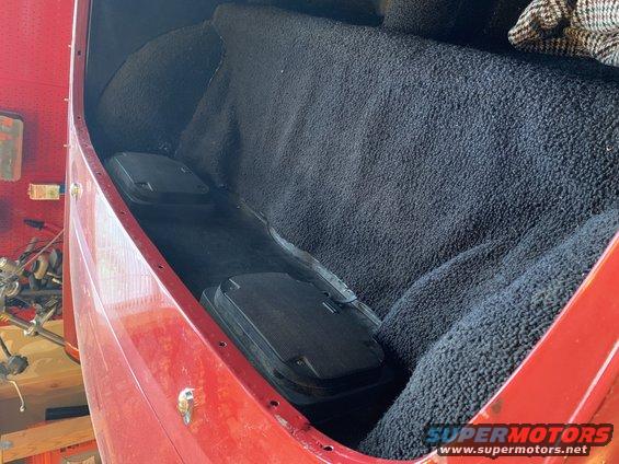 Red vehicle interior cargo area with black carpet and two black floor storage compartments