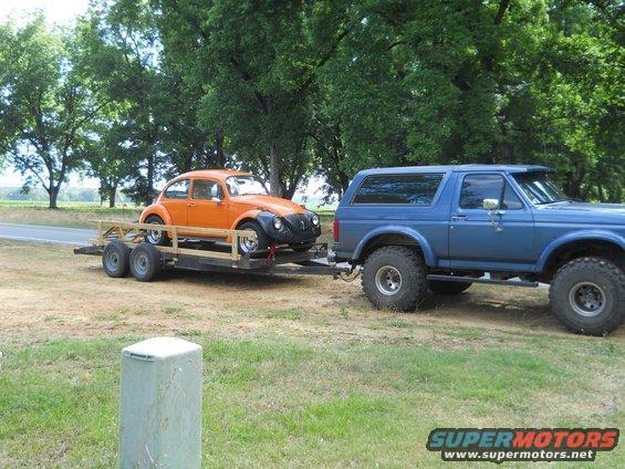 Blue 1992 Ford Bronco towing a trailer with an orange Volkswagen Beetle
