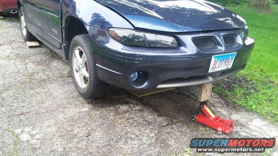 Blue Pontiac Grand Prix on a jack with wood blocks under the frame