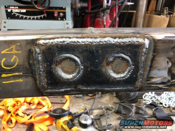 Welded frame section with two circular cutouts and yellow markings. Tools and straps are visible below