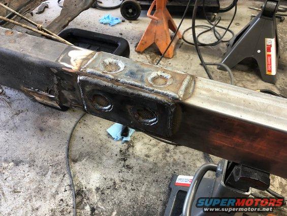 Close-up of a vehicle frame with fresh welds, supported by jack stands in a workshop