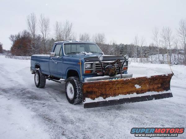 Blue pickup truck with a snow plow attached, parked on a snowy road
