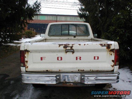 Rear view of a white Ford pickup truck with rust on the tailgate and red 'FORD' lettering