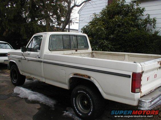 White pickup truck with rust spots on the rear fender, seen from the side