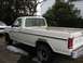 1986 Ford F-150 - A white pickup truck is parked next to another vehicle, showing its side profile with visible rust.