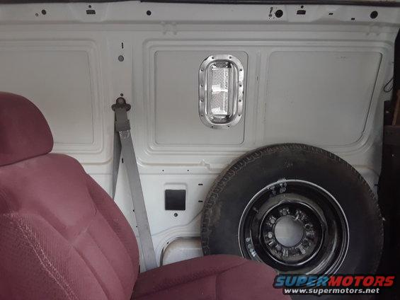 Van interior cargo area with maroon seat, spare tire, and a light fixture on the wall