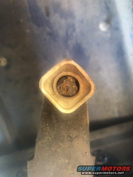 Close-up of a rusted bolt head inside a square plastic housing