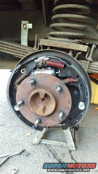 Rear drum brake assembly with brake shoes, springs, and wheel cylinder. Vehicle is supported by jack stands