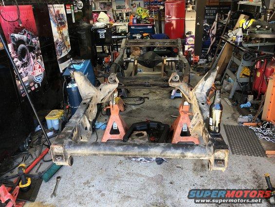 Jeep Wrangler frame assembly on orange jack stands in a garage, with tools and equipment in the background