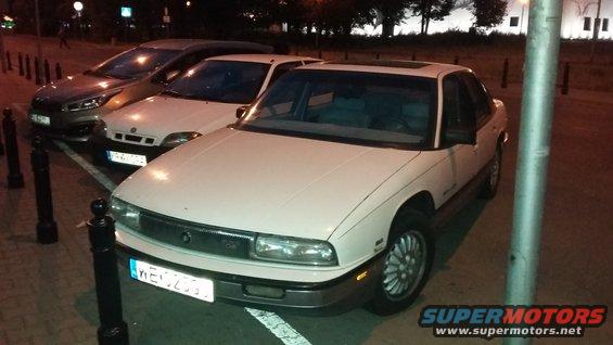 White sedan parked at night, front view. License plate visible