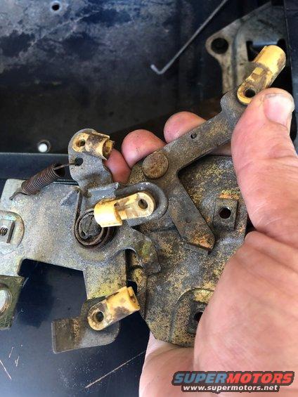 hand holding rusty tailgate latch assembly with yellow plastic parts and a spring