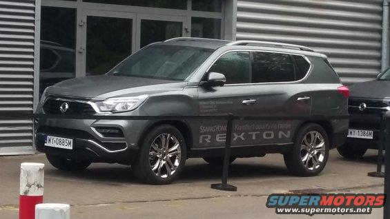 Gray SsangYong Rexton parked outside a building, with another vehicle visible to the right