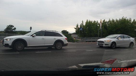 Two white cars on a road, one is an Audi A4 Allroad wagon, the other is a Ford Fusion sedan