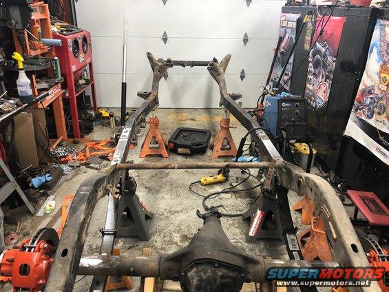 Vehicle frame on jack stands in a garage, showing rust and some new welds