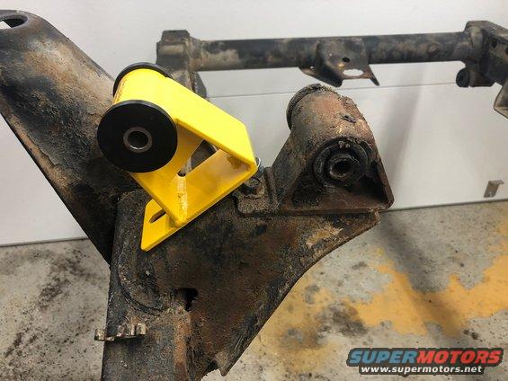 Yellow polyurethane bushing mount attached to a rusty metal frame component